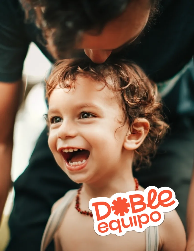 Niño sonriendo mientras una persona adulta le da un beso en la cabeza.